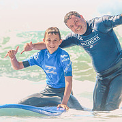 padre e figlio insieme al corso di surf per famiglie padre e figlio condividono la stessa esperienza surfando insieme nella lezione per famiglie